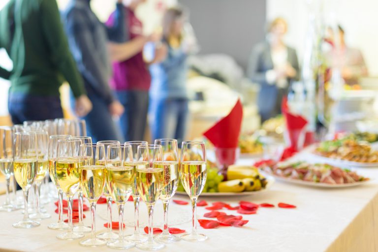 Banquet event. Table with the wineglasses, snacks and cocktails. People celebrating in the background.