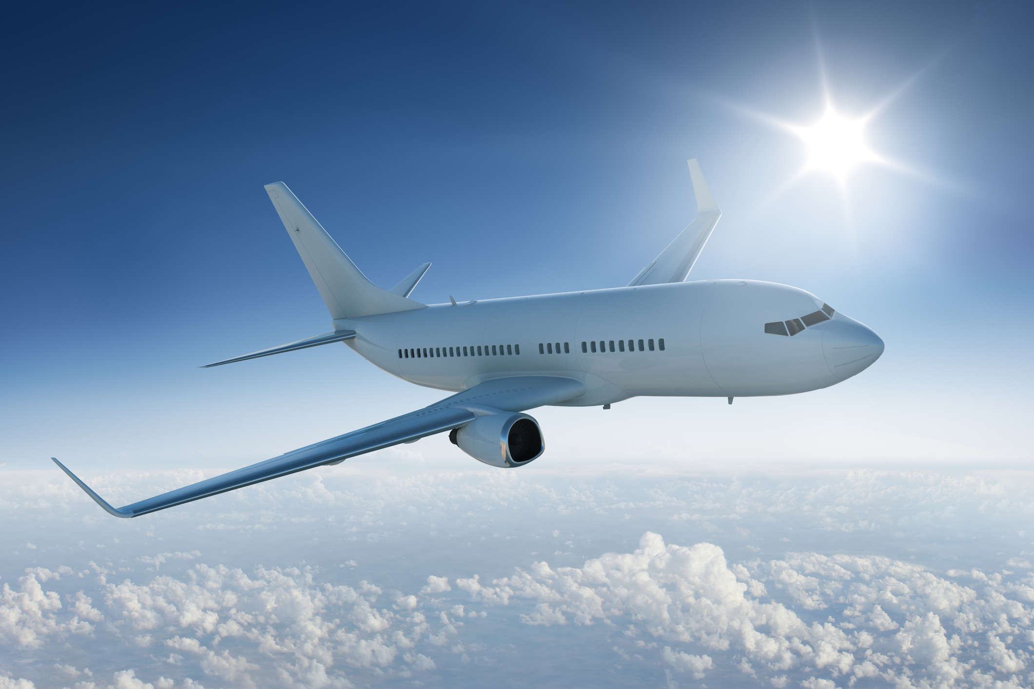 Airliner flying past the sun – in blue sky Airplane flies above the clouds in blue sky with sun in background.